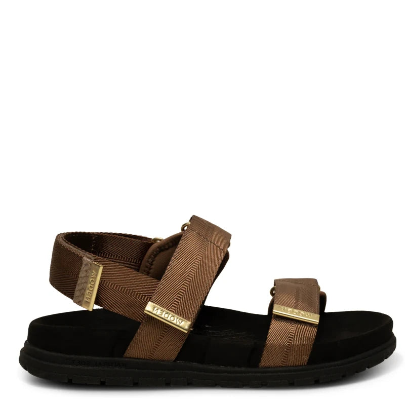En enkel, moderne sandal i brun med to brede remme — én over forfoden og én om anklen — monteret på en kontrastfuld, mørk sål.